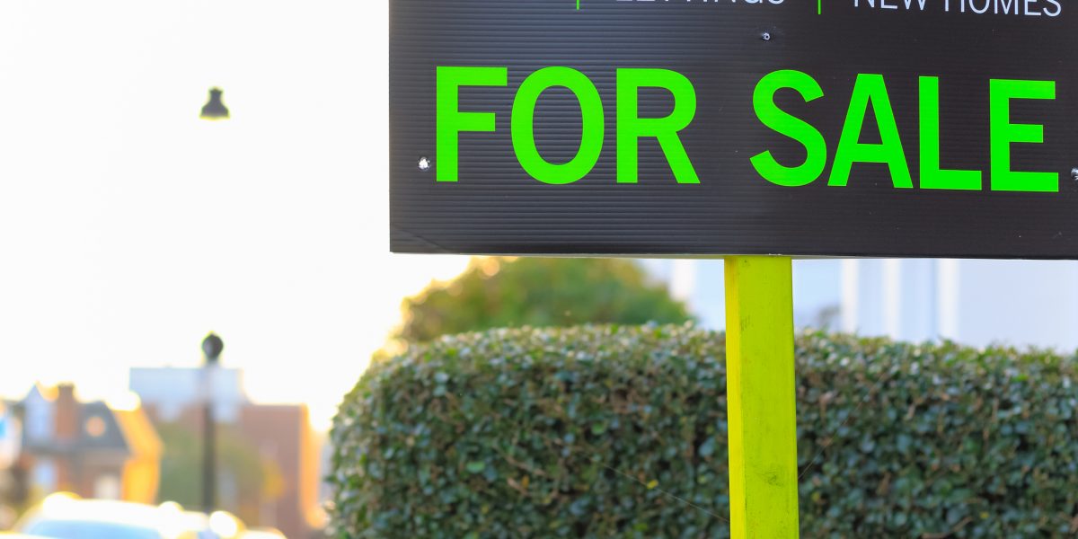 For Sale sign in front of a hedge